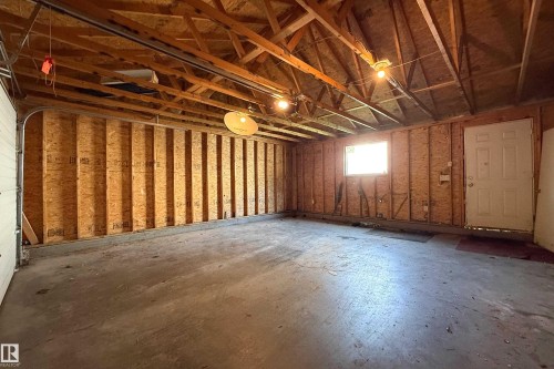 Spacious garage with exposed wood rafters, concrete flooring, overhead lighting, and a single window - 115 Griesbach Road Nw, Edmonton, AB - Indoor Photo Showing Basement