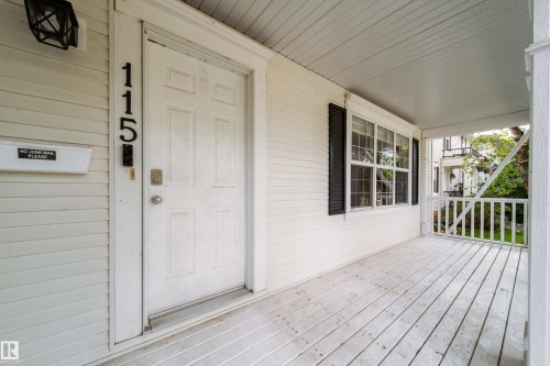 Covered front porch with white siding, panel door, and black window shutters - 115 Griesbach Road Nw, Edmonton, AB - Outdoor With Deck Patio Veranda With Exterior
