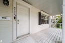 Covered front porch with white siding, panel door, and black window shutters - 115 Griesbach Road Nw, Edmonton, AB  - Outdoor With Deck Patio Veranda With Exterior 