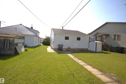 Grassed yard with a concrete pathway and two detached outbuildings - 4706 51 Ave, St. Paul Town, AB - Outdoor With Exterior