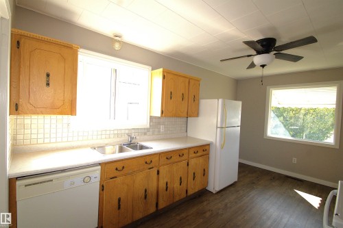Kitchen featuring wood cabinetry, a dual basin sink, white tile backsplash, and wood-finish flooring - 4706 51 Ave, St. Paul Town, AB - Indoor Photo Showing Kitchen With Double Sink