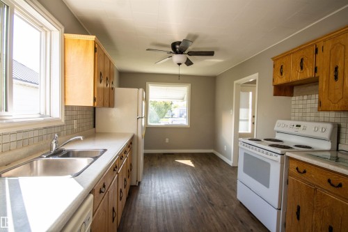 Kitchen featuring wood-finish flooring, light wood cabinetry, a double basin stainless steel sink, and a white tile backsplash - 4706 51 Ave, St. Paul Town, AB - Indoor Photo Showing Kitchen With Double Sink