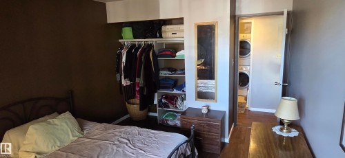 Built-in closet shelving with hanging rod, wood-finish flooring, and a dedicated laundry area with stacked appliances - #215 4404 122 St Nw, Edmonton, AB - Indoor Photo Showing Bedroom