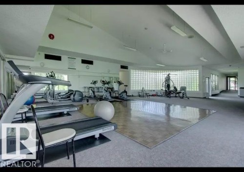 Fitness center featuring carpeted flooring, a wood-finish exercise mat area, and a curved glass block window wall - #215 4404 122 St Nw, Edmonton, AB - Indoor