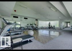 Fitness center featuring carpeted flooring, a wood-finish exercise mat area, and a curved glass block window wall - 