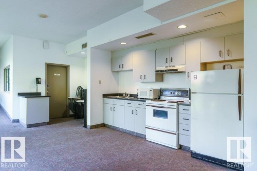 Galley kitchen featuring white cabinetry and appliances with dark countertops - #215 4404 122 St Nw, Edmonton, AB - Indoor Photo Showing Kitchen