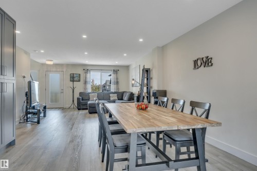 Open-concept living space featuring wood-finish flooring, recessed lighting, gray cabinetry, and a dining area with a wood-top table - #4 9250 156 Av Nw, Edmonton, AB - Indoor Photo Showing Dining Room