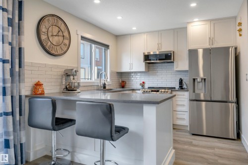 Kitchen featuring white cabinetry, subway tile backsplash, stainless steel appliances, recessed lighting, and wood-finish flooring - #4 9250 156 Av Nw, Edmonton, AB - Indoor Photo Showing Kitchen With Upgraded Kitchen
