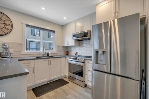 Modern kitchen featuring white cabinetry, stainless steel appliances, light wood-finish flooring, recessed lighting, and a subway tile backsplash - #4 9250 156 Av Nw, Edmonton, AB - Indoor Photo Showing Kitchen With Upgraded Kitchen