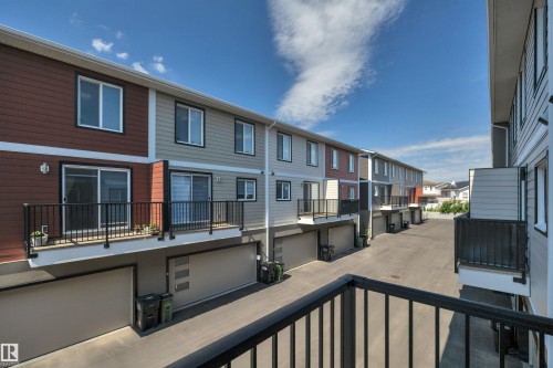 Multi-story townhome exterior featuring private balconies with black railings, individual garage doors, and varied siding finishes - #4 9250 156 Av Nw, Edmonton, AB - Outdoor With Exterior