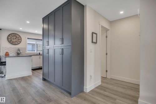 Expansive gray cabinetry with brushed nickel hardware, light wood-finish flooring, white kitchen island with countertop seating, white subway tile backsplash, and recessed lighting - #4 9250 156 Av Nw, Edmonton, AB - Indoor Photo Showing Other Room