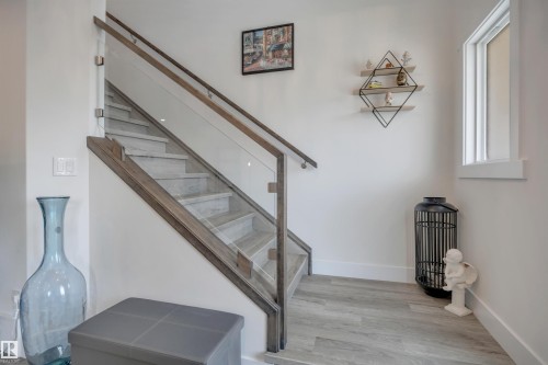 Staircase with wood-finish treads and glass panel railing - #4 9250 156 Av Nw, Edmonton, AB - Indoor Photo Showing Other Room