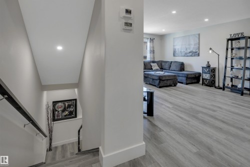 Staircase with modern handrail, recessed lighting, and wood-finish flooring extending into a spacious room - #4 9250 156 Av Nw, Edmonton, AB - Indoor Photo Showing Other Room