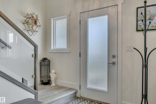 Entryway featuring a partially glazed door with privacy glass, a framed window, wood-finish flooring, and a glass-paneled staircase with dark railing - #4 9250 156 Av Nw, Edmonton, AB - Indoor Photo Showing Other Room