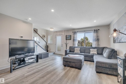 Spacious living area featuring wood-finish flooring, recessed lighting, and a large sliding glass door - #4 9250 156 Av Nw, Edmonton, AB - Indoor Photo Showing Living Room