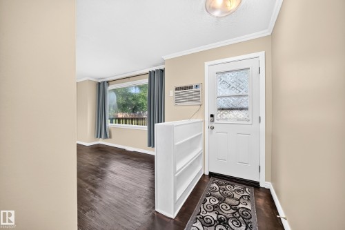 Entryway featuring a white door with decorative glass inserts, an air conditioning unit, and wood-finish flooring - 50 Rocque, Fort Saskatchewan, AB - Indoor Photo Showing Other Room