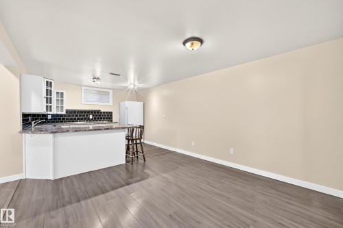 Kitchenette with white cabinetry, black subway tile backsplash, and a breakfast bar with a stone-finish countertop - 50 Rocque, Fort Saskatchewan, AB - Indoor Photo Showing Kitchen