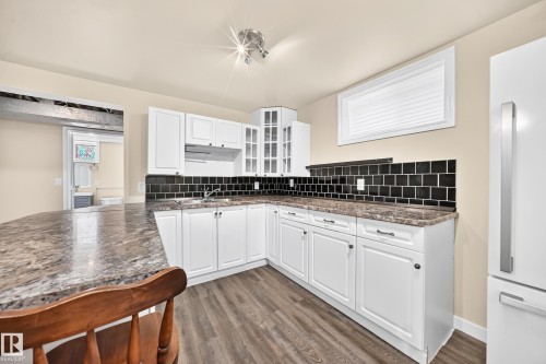 White cabinetry with dark hardware, dark tiled backsplash, wood-finish flooring, and a stone-finish countertop - 50 Rocque, Fort Saskatchewan, AB - Indoor Photo Showing Kitchen