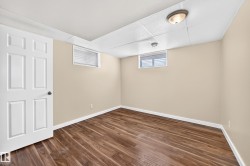 Finished basement room featuring warm beige walls, recessed ceiling lighting, and durable wood-finish flooring - 