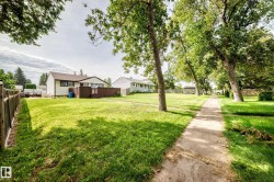 Expansive grassy yard with mature trees, a wooden privacy fence, and a concrete walkway - 