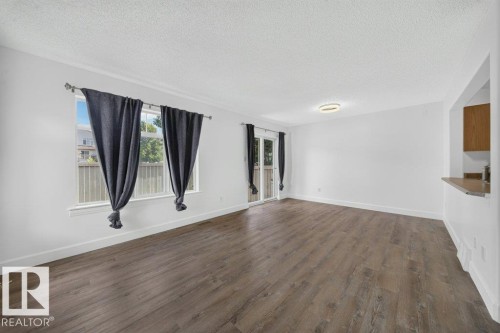 Wood-finish flooring, white walls, and a contemporary flush-mount ceiling light illuminate this open concept space - #47 30 Levasseur Rd, St. Albert, AB - Indoor Photo Showing Other Room