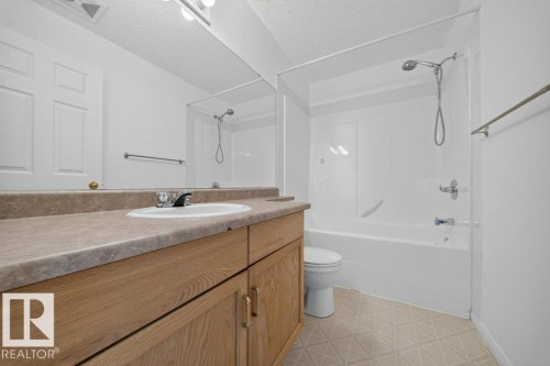 Bathroom featuring a tub/shower combination, light wood-finish vanity, integrated countertop sink, and patterned flooring - #47 30 Levasseur Rd, St. Albert, AB - Indoor Photo Showing Bathroom