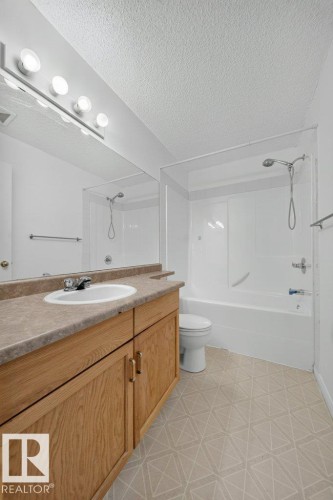 White vanity with a laminate countertop and integrated sink, full-width wall mirror, and a combination tub/shower with white surround - #47 30 Levasseur Rd, St. Albert, AB - Indoor Photo Showing Bathroom