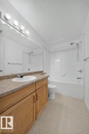 White vanity with a laminate countertop and integrated sink, full-width wall mirror, and a combination tub/shower with white surround - 