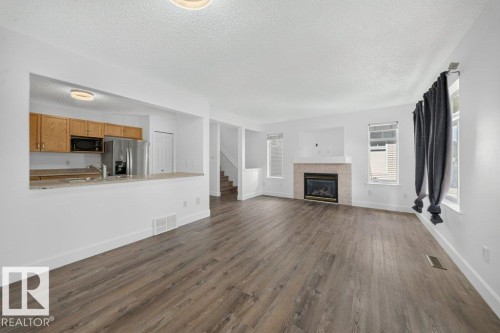 Wood-finish flooring throughout, fireplace with a stone surround, and an open concept kitchen with wood cabinetry - #47 30 Levasseur Rd, St. Albert, AB - Indoor With Fireplace