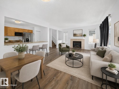 Open-concept design featuring wood-finish flooring, a kitchen with wood cabinetry and stainless steel appliances, a breakfast bar, and a fireplace with a stone surround - #47 30 Levasseur Rd, St. Albert, AB - Indoor With Fireplace