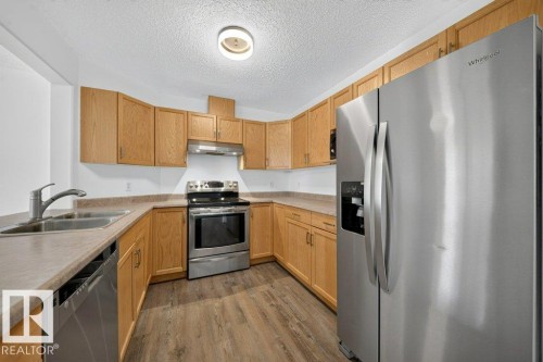 Kitchen featuring wood-finish cabinetry, stainless steel appliances, laminate countertops, and wood-finish flooring - #47 30 Levasseur Rd, St. Albert, AB - Indoor Photo Showing Kitchen With Double Sink