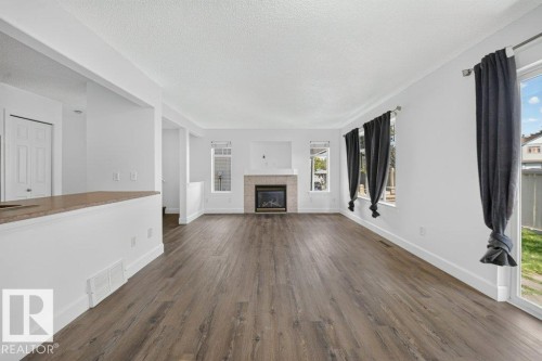 Spacious interior with wood-finish flooring, a contemporary fireplace, and multiple windows - #47 30 Levasseur Rd, St. Albert, AB - Indoor Photo Showing Living Room With Fireplace