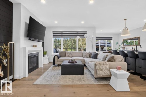 Open-concept living space with wood-finish flooring, a contemporary fireplace, recessed lighting, and large windows - 94 Harvest Crescent, Ardrossan, AB - Indoor Photo Showing Living Room With Fireplace