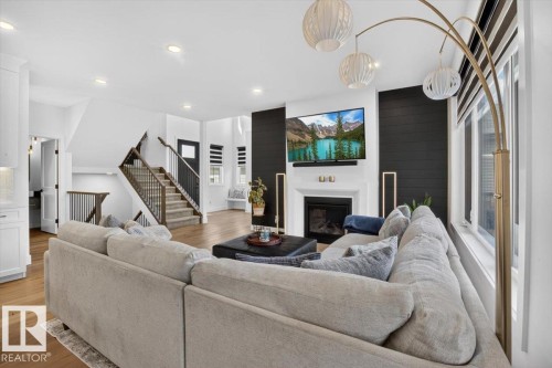 Wood-finish flooring throughout, a shiplap accent wall, fireplace with white mantel, recessed lighting, and a staircase with wood treads and metal balusters - 94 Harvest Crescent, Ardrossan, AB - Indoor Photo Showing Living Room With Fireplace
