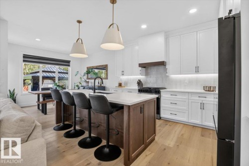 Gourmet kitchen with wood-finish flooring, white cabinetry, a large kitchen island, and under-cabinet lighting - 94 Harvest Crescent, Ardrossan, AB - Indoor Photo Showing Kitchen With Upgraded Kitchen