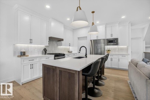 White upper and lower cabinetry, wood-finish flooring, white countertops, stainless steel appliances, and a kitchen island with a built-in sink - 94 Harvest Crescent, Ardrossan, AB - Indoor Photo Showing Kitchen With Stainless Steel Kitchen With Upgraded Kitchen