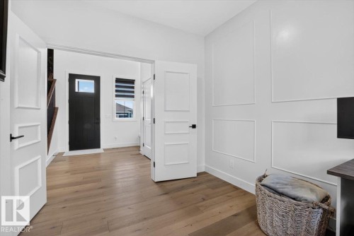 Light wood-finish flooring, white paneled accent wall, contemporary interior doors with matte black hardware, and an entryway with a dark-paneled door - 94 Harvest Crescent, Ardrossan, AB - Indoor Photo Showing Other Room