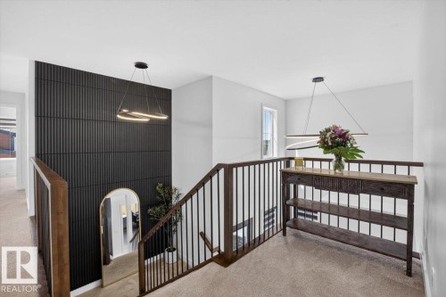 Feature wall with vertical paneling, contemporary hanging light fixtures, metal baluster railing, and natural wood handrails - 94 Harvest Crescent, Ardrossan, AB - Indoor Photo Showing Other Room