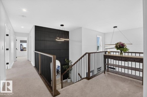 Upper-level landing with plush carpeting, contemporary linear chandeliers, and dark wood-tone railings with black metal spindles - 94 Harvest Crescent, Ardrossan, AB - Indoor Photo Showing Other Room