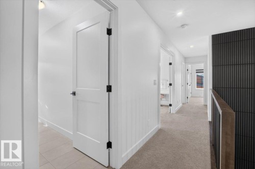 Hallway featuring neutral-toned carpeting, white interior doors with matte black hardware, and a textured dark accent wall - 94 Harvest Crescent, Ardrossan, AB - Indoor Photo Showing Other Room