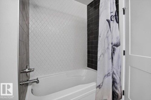 Bathtub with polished chrome fixtures, white scalloped tile surround, and contrasting dark tile accent wall - 94 Harvest Crescent, Ardrossan, AB - Indoor Photo Showing Bathroom