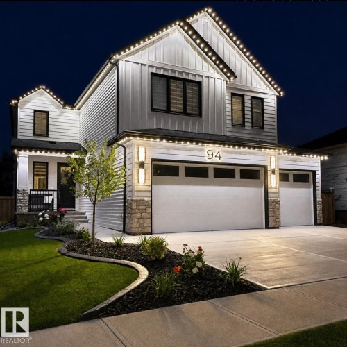 White siding exterior with board and batten accents, stone detailing, a two-car garage, and established landscaping - 94 Harvest Crescent, Ardrossan, AB - Outdoor With Facade