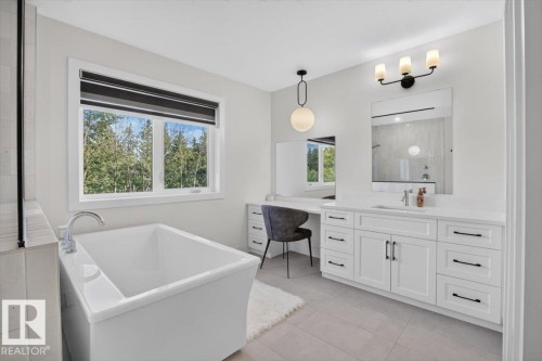 Freestanding soaking tub with polished chrome fixtures, expansive vanity with dual sinks, built-in makeup vanity, pendant lighting, and large format floor tiling - 94 Harvest Crescent, Ardrossan, AB - Indoor Photo Showing Bathroom