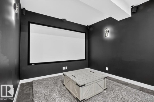 Media room featuring a large projection screen, dark wall finishes, wall sconces, ceiling-mounted speakers, and a carpeted floor - 94 Harvest Crescent, Ardrossan, AB - Indoor Photo Showing Other Room