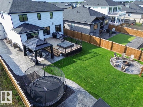 Expansive backyard featuring a manicured lawn, a large stamped concrete patio, a raised wood deck with a hot tub, a covered gazebo, and a circular fire pit area - 94 Harvest Crescent, Ardrossan, AB - Outdoor With Deck Patio Veranda With Exterior