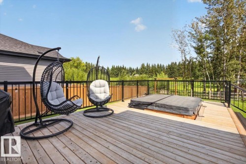 Expansive wooden deck featuring a built-in hot tub with cover, black metal railing, and a privacy fence - 94 Harvest Crescent, Ardrossan, AB - Outdoor With Deck Patio Veranda With Exterior