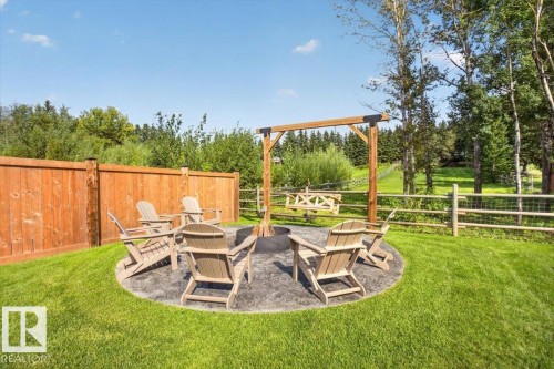 Outdoor fire pit area featuring a circular stamped concrete patio, wood-toned privacy fencing, and an adjacent swing frame - 94 Harvest Crescent, Ardrossan, AB - Outdoor With Deck Patio Veranda