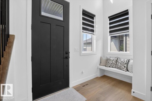 Black paneled entry door with transom window, wood-finish flooring, built-in window bench, and two windows with blinds - 94 Harvest Crescent, Ardrossan, AB - Indoor Photo Showing Other Room