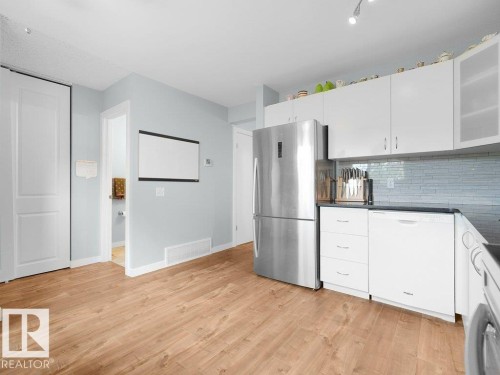 Wood-finish flooring, white cabinetry, stainless steel refrigerator, dark countertops, and a subway tile backsplash - #54 2131 Oak St, Sherwood Park, AB - Indoor Photo Showing Kitchen