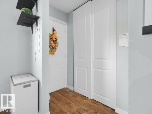 Wood-finish flooring with white baseboards, a paneled entry door, and white bi-fold closet doors - #54 2131 Oak St, Sherwood Park, AB - Indoor Photo Showing Other Room